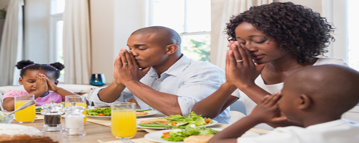 Happy family saying grace before meal at home in the kitchen